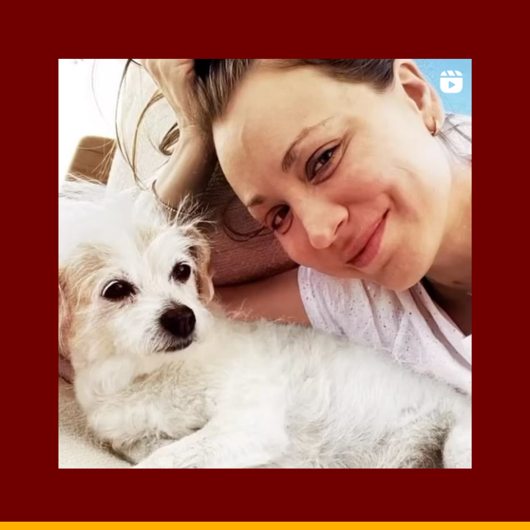 Kaley Cuoco smiling next to a small white dog lying down