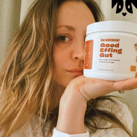 Actress Kaley Cuoco holding white jar labeled Good Effing Gut dog probiotic, close-up of face and product label